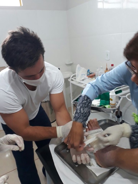 Male student nurse wraps Brazilian patient's foot.