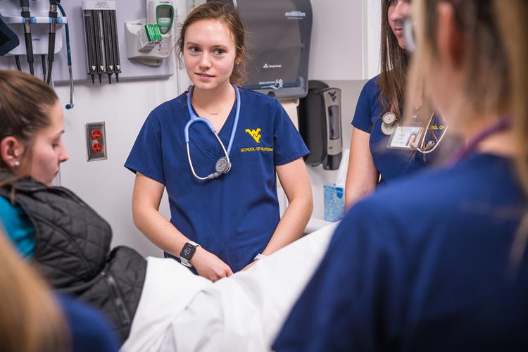A group of students gather around a volunteer standardized patient inside a WV STEPS exam area.