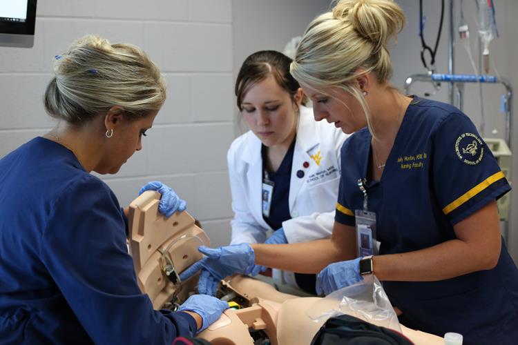 A Nursing student and two faculty members practice a procedure on a manakin.