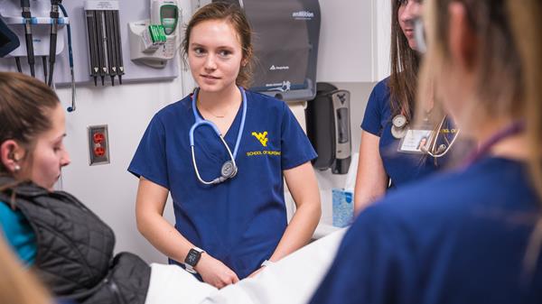 A group of students gather around a volunteer standardized patient inside a WV STEPS exam area.