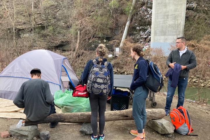 Student teams work outdoors with an individual experiencing homelessness outside of a tent.