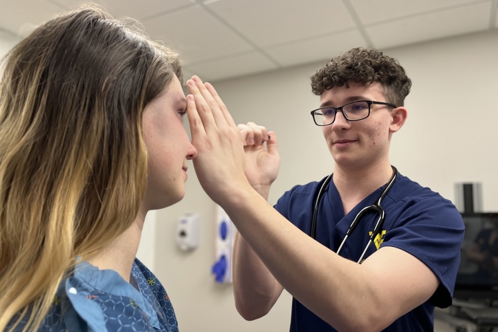 Male nursing student uses penlight to examine a patient in an exam room.