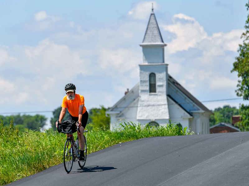 A cyclist rides on a quiet country road near a quiet country church.
